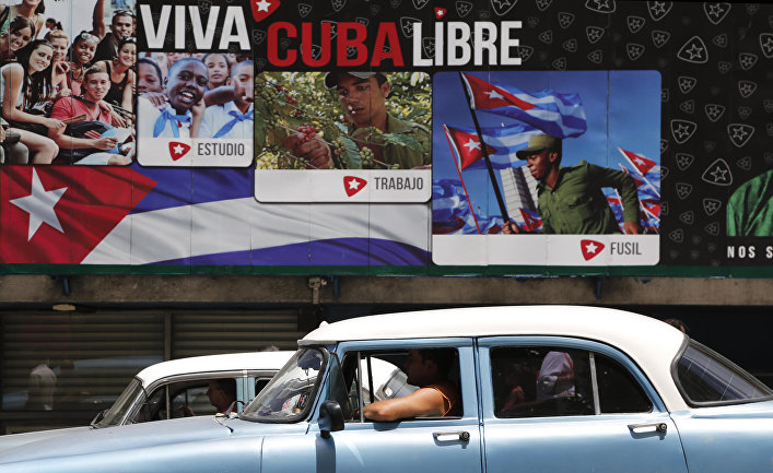 A classic American car passes in front of some signs that reads in Spanish "Long Live Free Cuba" in Havana, Cuba