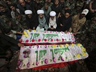 Mourners and militiamen pray around the flag-draped coffins of two members of the Peace Brigades