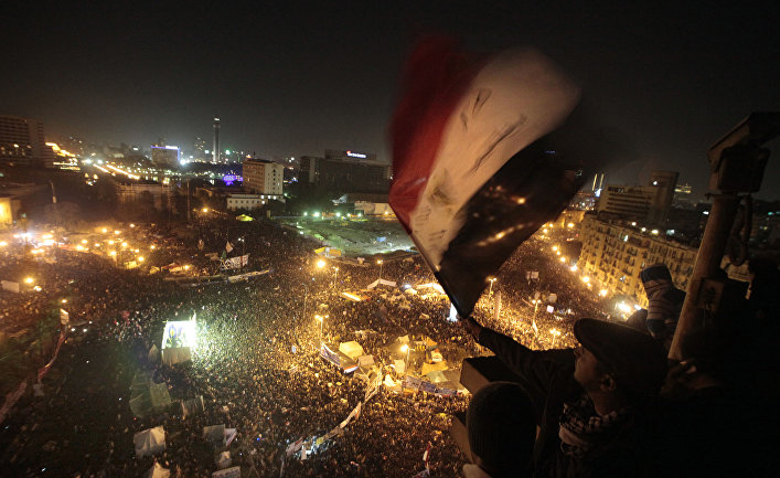An Egyptian waves the national flag as he and others watch thousands of people gather in Tahrir Square to mark the first anniversary of the popular uprising that unseated President Hosni Mubarak, Cairo, Egypt, Wednesday, Jan. 25, 2012