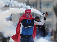 A Palestinian demonstrator uses a slingshot to throw back a tear gas canister at Israeli troops following a rally marking the 48th anniversary of the Popular Front for the Liberation of Palestine (PFLP), in the West Bank