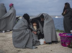 A family tries to keep warm with blankets, after the boat on which they crossed a part of the Aegean sea from Turkey hit on rocks, on the Greek island of Lesbos, on Saturday, Dec. 12, 2015